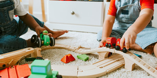 Anschnitt von zwei Kleinkindern, die auf einem Teppich mit einer Holzeisenbahn spielen