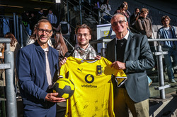 Auf dem Foto sieht man, wie Prof. Manfred Bayer gemeinsam mit zwei anderen Männern ein Trikot in der Hand hält und für ein Foto in die Kamera lächelt.