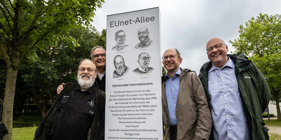 Stele vier Männer stehen draußen vor einer weißen Stele, auf der ihre Gesichter (in einem Fall das des Vaters) gezeigt sind
