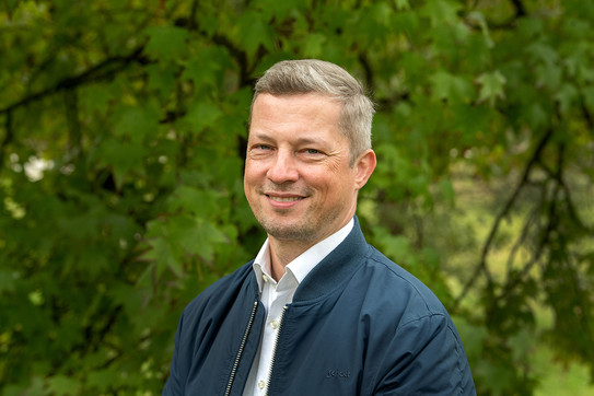 Portrait photo of Prof. Matthias Kortmann: Prof. Kortmann is wearing a light-colored shirt and a dark jacket and smiling at the camera.