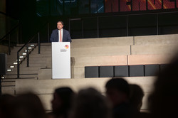 Photo: A person speaks at a podium on a stage.