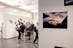 Mehrere weiße Wände, auf denen verschiedene Bilder angebracht sind. Dazwischen stehen Besucher*innen der Ausstellung.