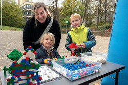 Das Bild zeigt zwei Kinder und eine Frau, die hinter einem schwarzen Tisch mit Lego stehen. Im Hintergrund ist der Campus Nord und ein Gebäude der TU Dortmund zu sehen.