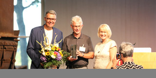 Dortmund Dialogue Award 2022 Two men and a woman stand on a stage for an award ceremony.