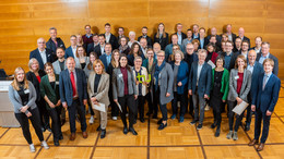 April Zu sehen ist die Gruppe an Stifter*innen bei der Stipendienfeier. Eine Person in de Mitte hält das grüne TU-Logo in der Hand.