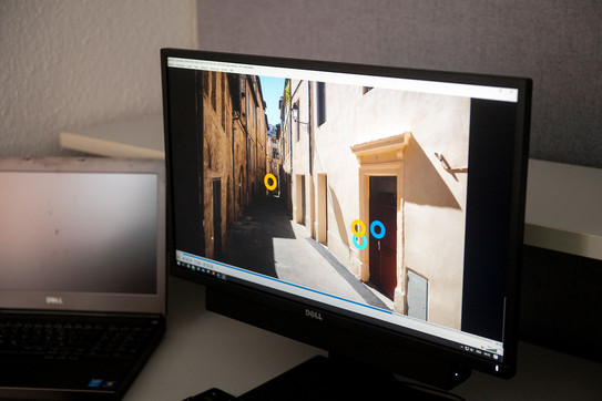 Ein Computerbildschirm zeigt die Außenansicht einer schmalen Gasse mit Häuserfassaden. Ein Eye-Tracking-Programm hat auf dem Bild Punkte in Augenhöhe eines Fußgängers markiert.