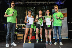 Auf der Bühne stehen die drei schnellsten Läuferinnen der Kategorie 5-Kilometer-Lauf und die zwei Moderatoren