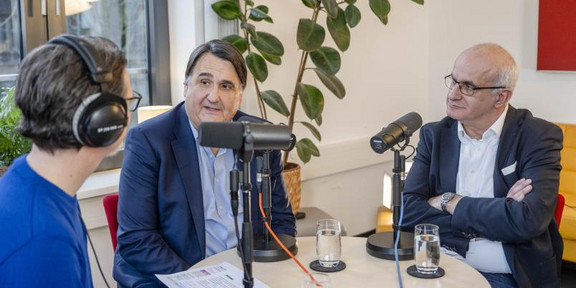 Aufnahmesituation eines Podcasts: Drei Männer sitzen an einem runden Tisch.
