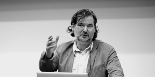 Foto in schwarz-weiß: Prof. Bastiaens steht an einem Redepult und gestikuliert.