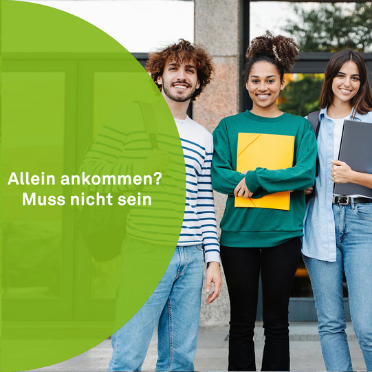 Eine kleine Gruppe von Studierenden steht mit Unterlagen in der Hand vor einem Gebäude. Sie lächeln in die Kamera. Auf der linken Seite ist ein grüner Halbkreis mit der Aufschrift "Allein ankommen? Muss nicht sein."