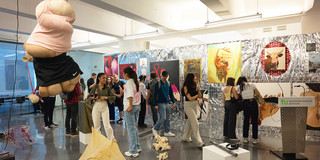 Ein Ausstellungsraum mit verschiedenen Installationen und Kunstwerken. Zwischen den Kunstwerken stehen verschiedene Menschen, die diese betrachten.
