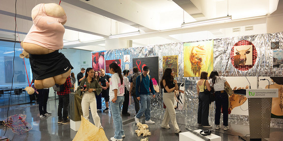 Ein Ausstellungsraum mit verschiedenen Installationen und Kunstwerken. Zwischen den Kunstwerken stehen verschiedene Menschen, die diese betrachten.
