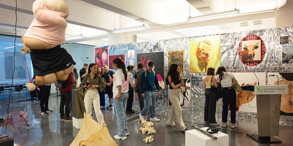 Ein Ausstellungsraum mit verschiedenen Installationen und Kunstwerken. Zwischen den Kunstwerken stehen verschiedene Menschen, die diese betrachten.