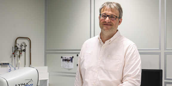 Prof. Andreas Jung Ein Mann in einem hellen Hemd steht in einem Labor und lächelt in die Kamera.