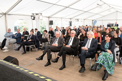 A tent filled with people sitting on chairs, facing the lectern and listening.