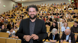 Das Bild zeigt ein Porträtfoto von Prof. El-Mafaalani bei seiner Antrittsvorlesung an der TU Dortmund. Im Hintergrund ist der Hörsaal mit Publikum zu sehen.