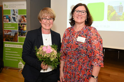 Zwei Frauen stehen nebeneinander und posieren für ein Foto. Die Frau auf der linken Seite hält einen Blumenstrauß in der Hand.