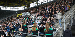 Die mit Erstsemestern besetzte Tribüne. Im Vordergrund Cheerleader, die zu einer LaOla-Welle animieren.