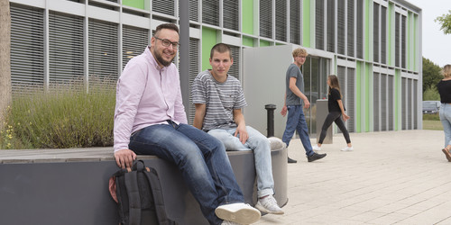 Studierende sitzen vor einem Gebäude.
