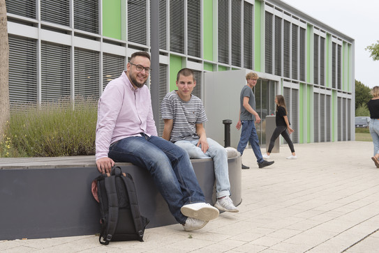 Studierende sitzen vor einem Gebäude.