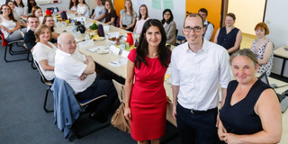 Sprachbrücken Im Vordergrund stehen zwei Frauen und ein Mann, dahinter sitzen Personen an einem Tisch