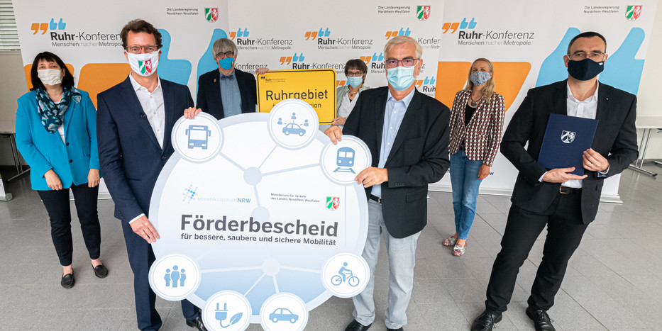 Zu sehen sind mehrere Erwachsene mit Masken. Zwei Männer halten ein Plakat hoch. Im Hintergrund sind Banner mit der Aufschrift Ruhr-Konferenz zu sehen.