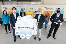 Zu sehen sind mehrere Erwachsene mit Masken. Zwei Männer halten ein Plakat hoch. Im Hintergrund sind Banner mit der Aufschrift Ruhr-Konferenz zu sehen.
