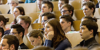 Studierende im Hösraal, Junge Frau im Fokus, die den Kopf auf beide Arme stüzt