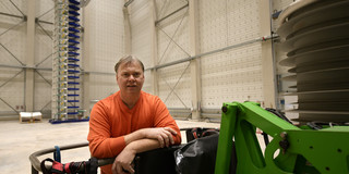 Impulsgenerator Ein Mann lehnt sich an eine große Maschine, er steht in einer Halle.