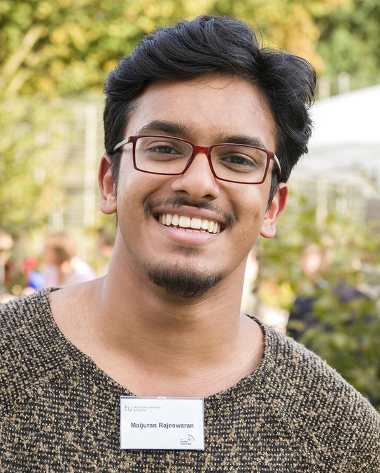 Foto eines lächelnden Stipendiaten und er trägt einen Pullover mit einem Namensschild