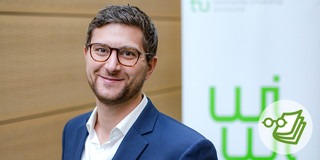 Foto: Eine Person steht vor einer Wand und einem Banner mit dem Logo der TU Dortmund Universität.