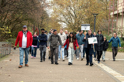 Das Bild zeigt eine große Gruppe von Personen, die über den Campus Nord der TU Dortmund laufen. Geführt wird die Gruppe von einer Person, die ein Plakat mit der Aufschrift "Roboterfußball" hält.