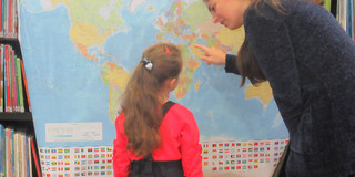 Ein Kind und eine erwachsene Frau stehen vor einer Weltkarte.