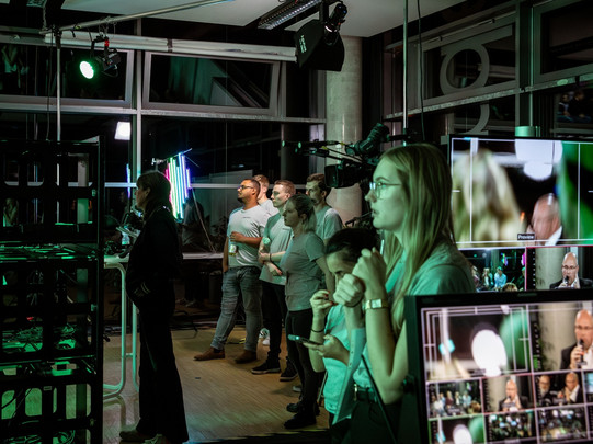 Foto: Mehrere Menschen stehen in einem Raum mit Technik, Monitoren und Studiolicht.