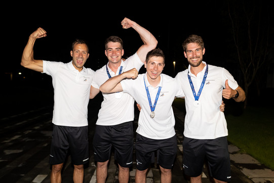 Four men in white shirts and black pants cheer.
