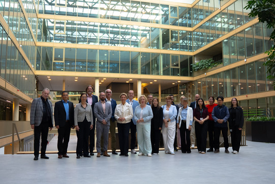 Eine größere Gruppe von Frauen und Männern steht für ein gemeinsames Foto in einem weitläufigen, modernen Atrium mit Glas und Holz. Die Personen stehen in einer Reihe und blicken in die Kamera.