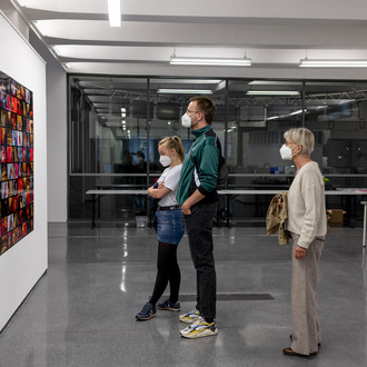 Drei Personen schauen sich Ausstellungsobjekte an einer Wand an