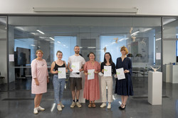 Ausstellung „Rundgang Kunst“ Mehrere Personen stehen vor einer Glaswand in einer Reihe und halten Urkunden in den Händen.
