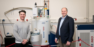 Two researchers stand next to a laboratory apparatus. 