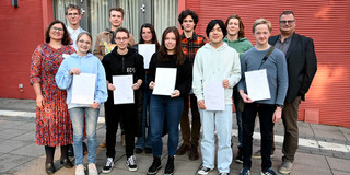 Neun Jugendliche halten Urkunden in den Händen und posieren für ein Gruppenfoto. Drei Erwachsene stehen links und rechts von der Gruppe.