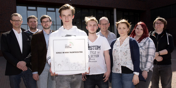 Talentscouting Gruppenfoto mit Plakette, im Hintergrund ist Name des Berufskollegs zu lesen