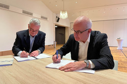 Unterschrift Erich Dreier und Manfred Dreier Zwei Männer, die in einem großen Raum jeweils einen Vertrag unterschreiben.