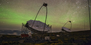 Foto: Zwei große Teleskope stehen unter einem klaren, sternenübersäten Himmel mit grünlichem Schimmer.