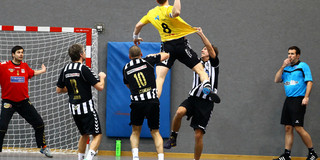 Handball A handball player jumps in the air to throw a goal, players of the opposing team try to stop him from doing so