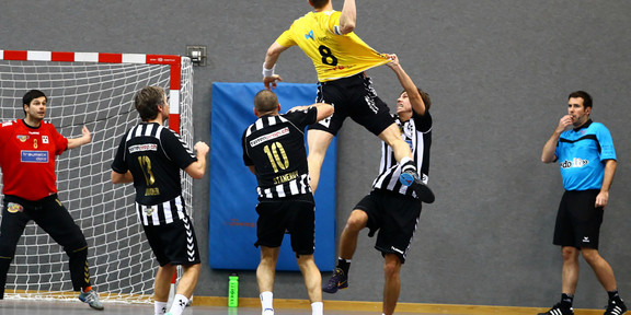 Handball Ein Handballspieler springt in die Luft, um ein Tor zu werfen, Spieler der gegnerischen Mannschaft versuchen, ihn davon abzuhalten
