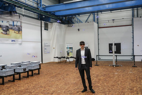 Ein Mann mit einer speziellen Brille steht in einer Versuchshalle, um ihn herum fliegen Drohnen