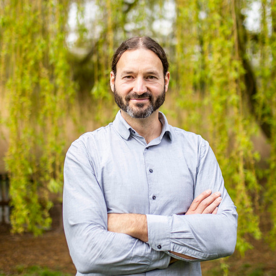 Portrait of a man in a shirt in front of a green tree