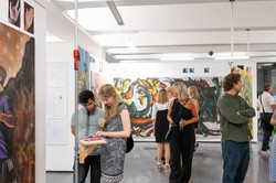 Auf dem Bild sind verschiedene Menschen zu sehen, die sich gemalte Bilder in einem Ausstellungsraum angucken.