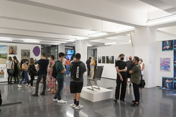 Mehrere Personen stehen in einer Halle einer Kunstausstellung und an den Wänden hängen Bilder.