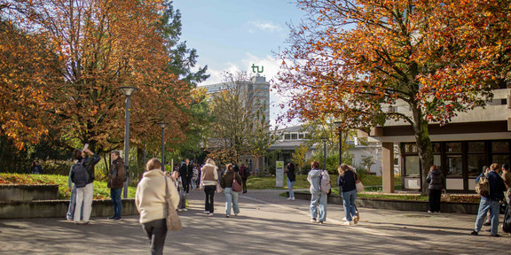 Foto: Ein Foto vom Campus der TU Dortmund im Herbst. Auf dem Foto sind Studierende, Food Fakultät und der Mathetower mit dem TU Logo zu sehen.